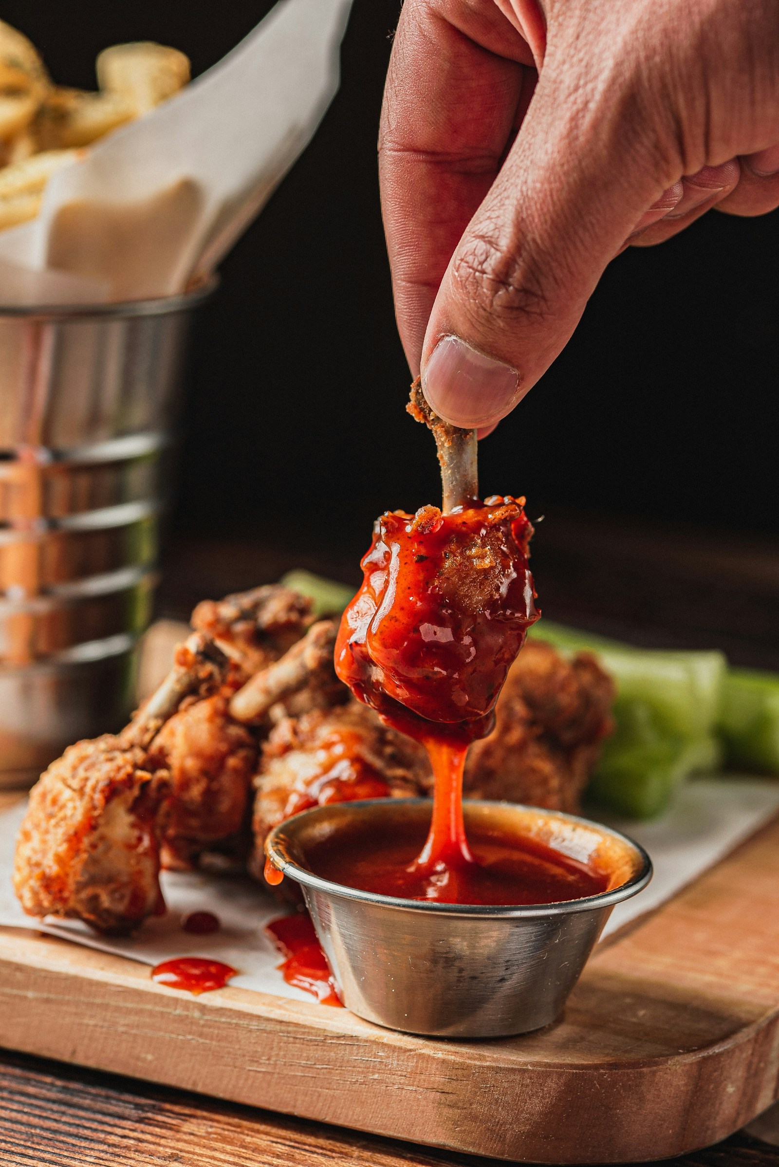 A chicken wing being dipped into barbecue sauce beside a meal
