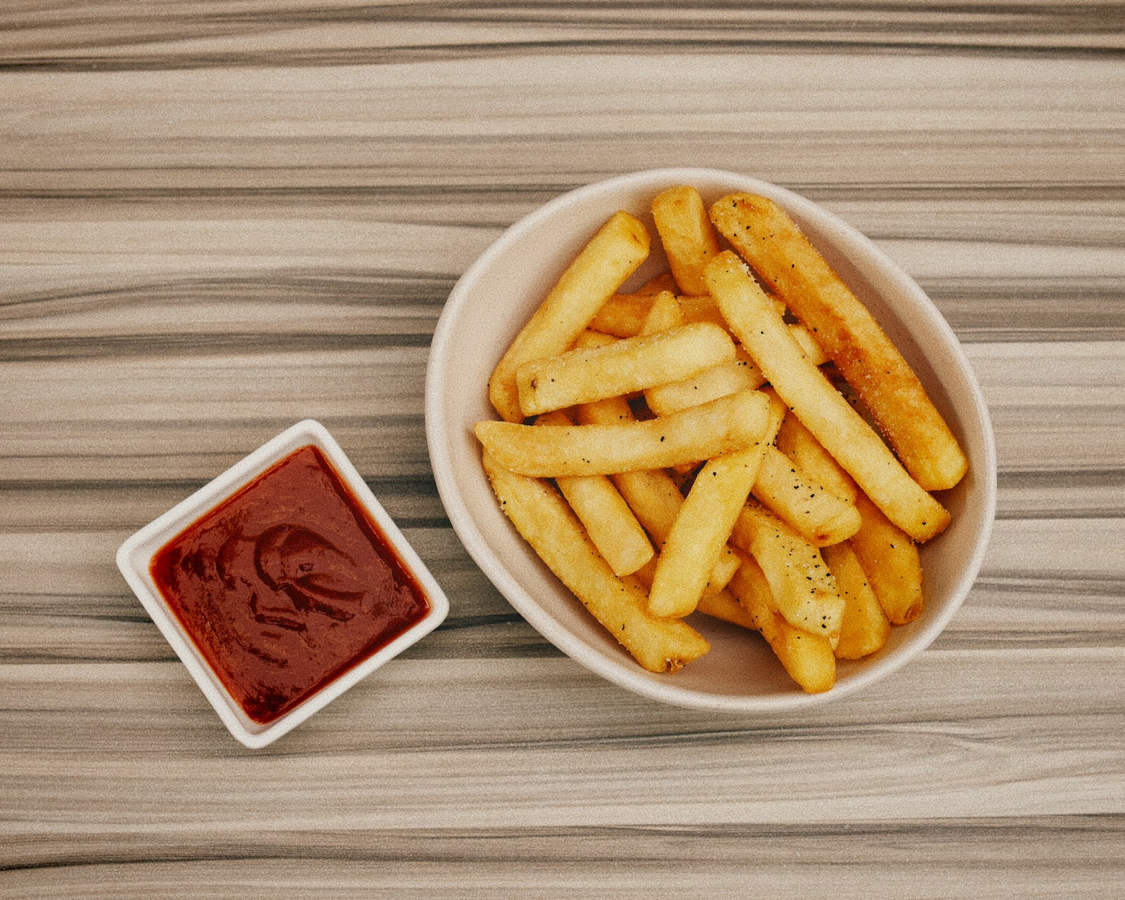 Golden French fries served with tomato ketchup on a wooden table